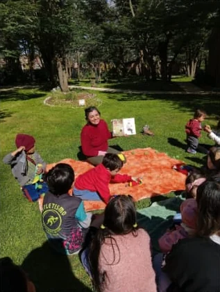 Maritza lee un cuento a niñas y niños sentados sobre una manta en el pasto