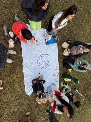 Vista desde arriba: familias alrededor de una tela blanca donde pintan juntas una espiral