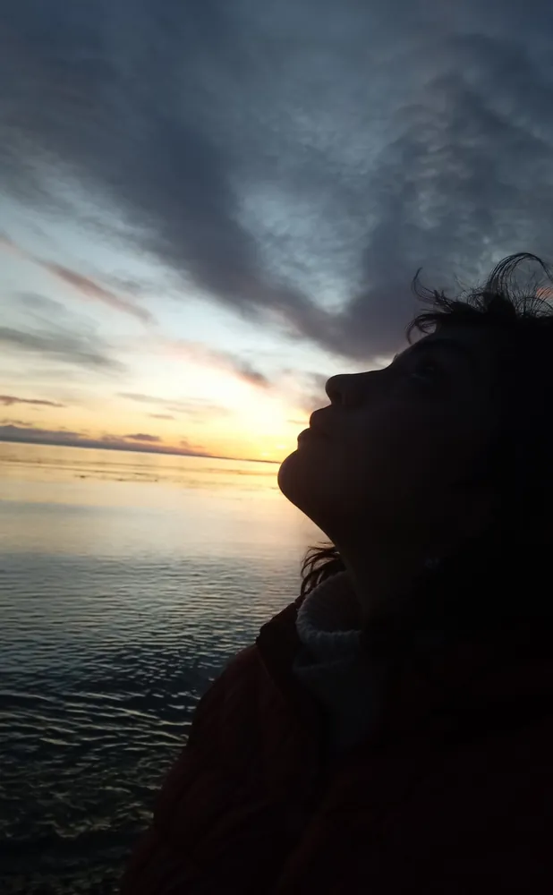 Maritza Rivas de perfil, mirando el cielo al atardecer frente al mar